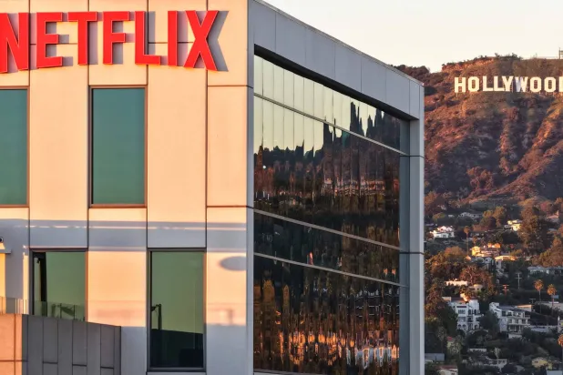 شعار «نتفليكس» معروض في استوديوهاتها مع لافتة هوليوود في الأفق (أ.ف.ب)