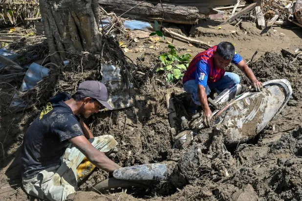 أشخاص يزيلون الطين من دراجة نارية إثر فيضانات مفاجئة في ميوريدو بمقاطعة بيدي جايا - إقليم آتشيه الإندونيسي (أ.ف.ب)