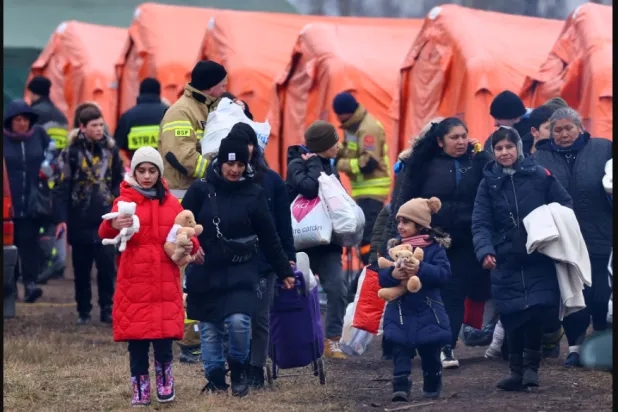 أشخاص يمرون بجوار الخيام في طريقهم للصعود إلى القطار بعد عبورهم الحدود من أوكرانيا إلى بولندا وسط الغزو الروسي (رويترز)