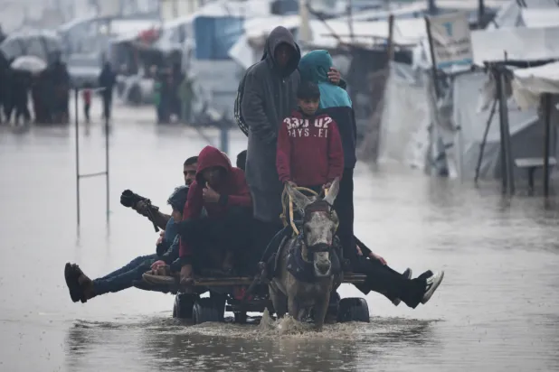 Palestinians cross a flooded street following heavy rain in Khan Younis, southern Gaza Strip, Thursday, Dec. 11, 2025. (AP Photo/Abdel Kareem Hana)