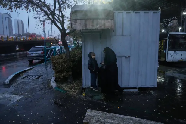 إيرانية تحتمي مع حفيدها من المطر في أحدر شوارع طهران الأربعاء (أ. ب)