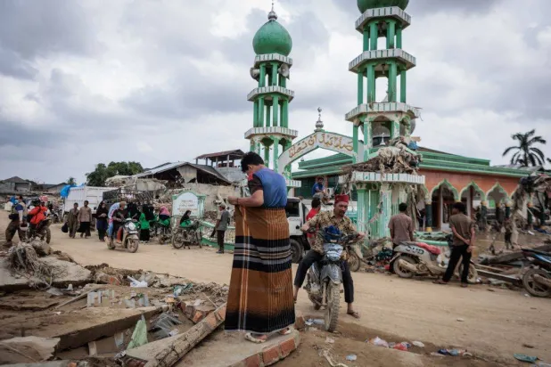 رجل يستعد لأداء صلاة الجمعة أمام مسجد الإحسان الذي دمرت الفيضانات جزءاً منه في آتشيه تاميانغ بإندونيسيا (أ.ف.ب)