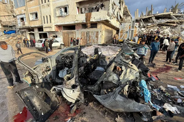 فلسطينيون يعاينون حطام سيارة استهدفتها ضربة إسرائيلية في مدينة غزة أمس (رويترز)