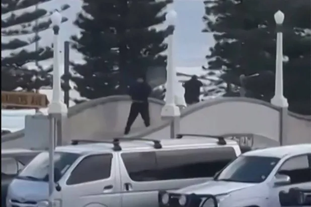 This screen grab made from UGC handout video footage courtesy of Timothy Brant-Coles shows two gunmen dressed in black firing multiple shots on a bridge at Bondi Beach in Sydney on December 14, 2025. (Photo by Handout / various sources / AFP)