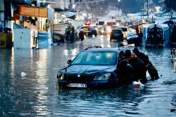 Şiddetli yağışlar nedeniyle meydana gelen sel sularının içinde kalmış bir arabayı iten yerlerinden edilmiş Filistinliler (AFP)