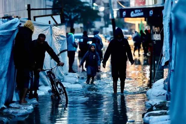 نازحون يمرون عبر برك المياه جراء الأمطار الغزيرة في مدينة غزة أمس (أ.ف.ب)