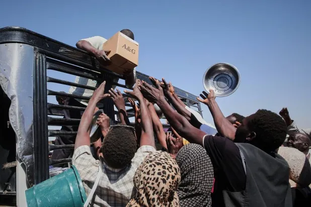 Sudanese families displaced from el-Fasher reach out as aid workers distribute food supplies at the newly established El-Afadh camp in Al Dabbah, in Sudan's Northern State, Sunday, Nov. 16, 2025. (AP)