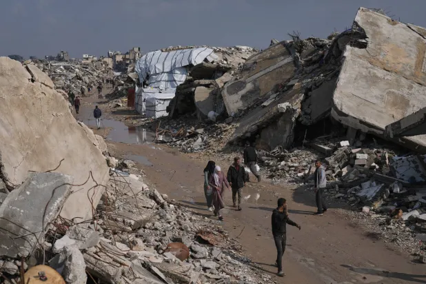 فلسطينيون يسيرون في شارع محاط بمبانٍ دُمّرت خلال العمليات الجوية والبرية الإسرائيلية في مدينة غزة، 17 ديسمبر 2025 (أ.ب)
