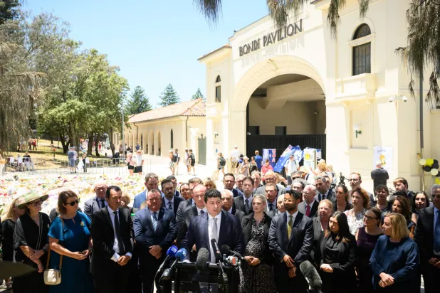 يتحدث عمدة ويفرلي ويل نيمي (في الوسط) إلى وسائل الإعلام بعد وضع إكليل من الزهور على نصب تذكاري مؤقت من الزهور في شاطئ بونداي بمدينة سيدني في أستراليا في 18 ديسمبر 2025... وتعيش أستراليا حالة حداد في أعقاب هجوم استهدف احتفالات الجالية اليهودية بعيد حانوكا في 14 ديسمبر في شاطئ بونداي والذي أسفر عن مقتل 16 شخصاً على الأقل بينهم مسلح واحد (إ.ب.أ)