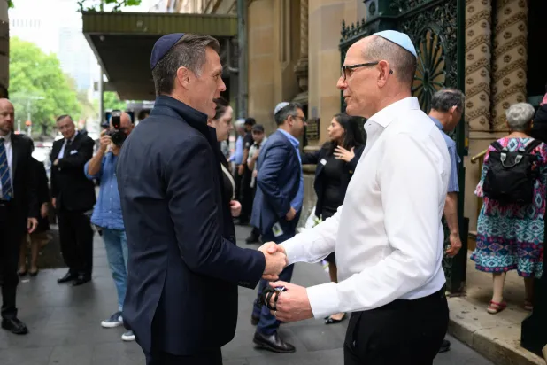 استقبل لاري دورفان المدير العام لكنيس غريت رئيس وزراء ولاية نيو ساوث ويلز كريس مينز لدى وصوله إلى الكنيس في سيدني 19 ديسمبر 2025 (إ.ب.أ)