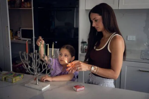 ريبيكا دي فيرولي مع ابنتها كلوي وهما تُجهّزان الشمعدان العائلي في منزلهما في نورث بونداي يوم الأحد (نيوريوك تايمز)