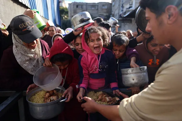 أطفال ينتظرون الحصول على نصيبهم من الطعام بمخيم النصيرات في غزة (أ.ف.ب)