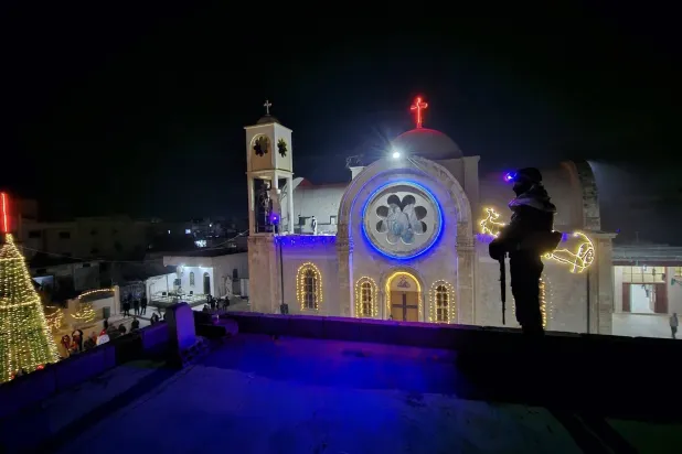 عنصر أمن سوري على سطح يطل على كنيسة القصير أثناء الاحتفال بإنارة شجرة الميلاد (متداولة)