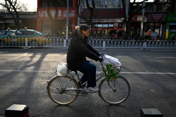 رجل يحمل مشتروات البقالة على دراجة في أحد شوارع العاصمة الصينية بكين (أ.ف.ب)