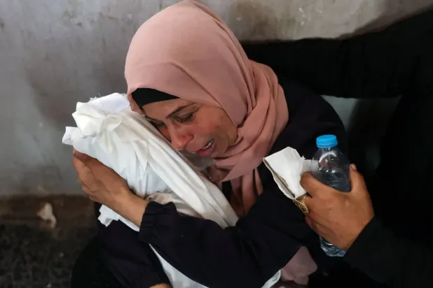 Filistinli bir kadın, Gazze şehrinde İsrail hava saldırısında öldürülen bir bebeği kucağında tutarken ağlıyor (AFP)