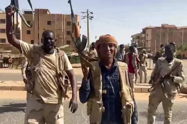 In this image grab taken from handout video footage released by the Sudanese paramilitary Rapid Support Forces (RSF) on April 23, 2023, fighters wave assault rifles as they cross a street in the East Nile district of greater Khartoum.  (Photo by Rapid Support Forces (RSF) / AFP)  