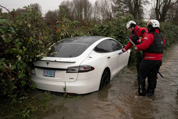 عناصر من إدارة الطوارئ الأميركية يفحصون سيارة «تسلا» خالية خلال فيضان غرين ريفر في واشنطن (رويترز)