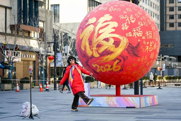 سيدة تستعد لالتقاط صورة تذكارية مع زينة العام الجديد في أحد الشوارع التجارية بالعاصمة الصينية بكين (أ.ف.ب)