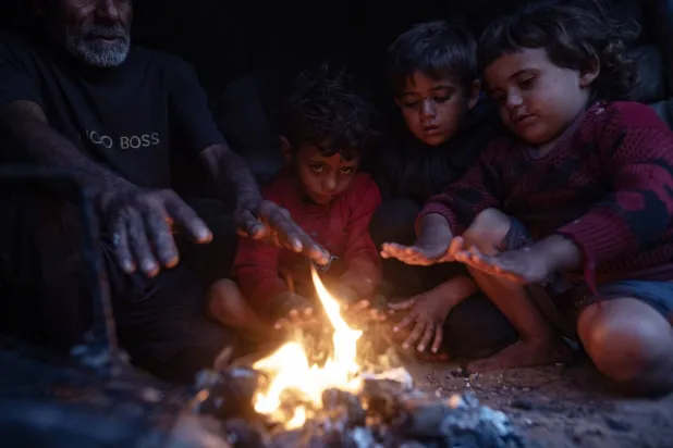 أفراد عائلة فلسطينية نازحة يتدفأون حول نار خارج مأواهم في مدينة خان يونس أمس (إ.ب.أ)