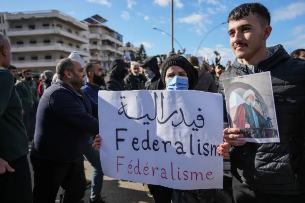 متظاهر في مدينة اللاذقية يحمل لافتة تطالب بفيدرالية في الساحل السوري في حين يتجمع أفراد من «الطائفة العلوية» للاحتجاج على تفجير مسجد حمص (إ.ب.أ)