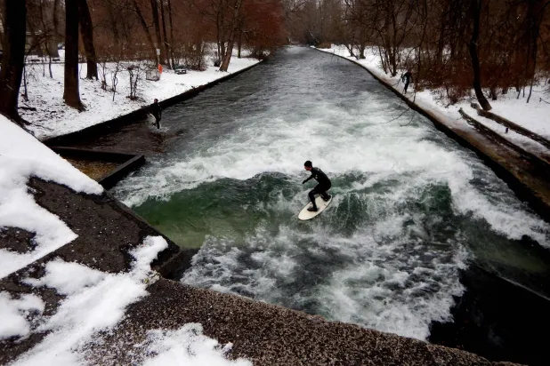 (FILES) Surfers ride the Eisbach (ice creek) wave during freezing conditions on the Isar River in the English Garden in Munich, southern Germany on January 4, 2017. (Photo by Mark RALSTON / AFP)