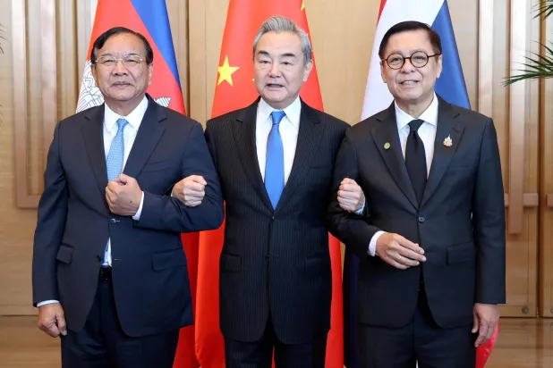 This handout photo taken and released by Agence Kampuchea Press (AKP) on December 29, 2025 shows China's Foreign Minister Wang Yi (C), Cambodia's Deputy Prime Minister Prak Sokhonn (L), who is also the country's Foreign Minister, and Thailand's Foreign Minister Sihasak Phuangketkeow (R) linking arms during a meeting in China's Yunnan province. (Handout / Agence Kampuchea Press (AKP) / AFP) 