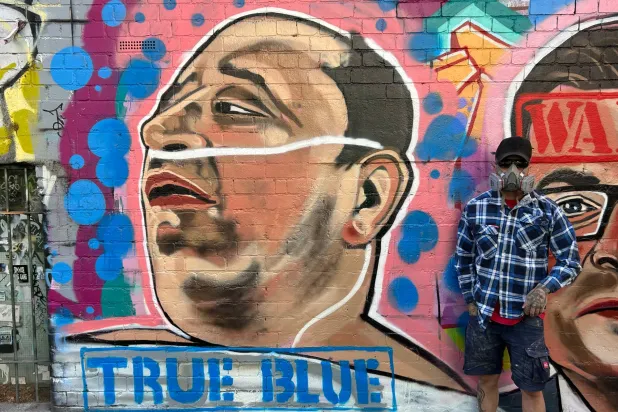 يقف فنان الشارع جارود جريش لالتقاط صورة بجانب لوحته التي تصور أحمد الأحمد وهو صاحب متجر سوري أسترالي يبلغ من العمر 43 عاماً والذي نزع سلاح أحد مهاجمي حادثة إطلاق النار في شاطئ بونداي بسيدني في ملبورن أستراليا (أ.ب) 