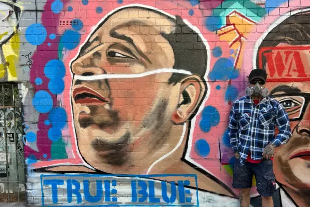 Sokak sanatçısı Jarrod Grech, Bondi Plajı'nda meydana gelen silahlı saldırıda saldırganlardan birini etkisiz hale getiren 43 yaşındaki Suriye asıllı Avustralyalı esnaf Ahmed el-Ahmed'i resmettiği duvar resminin yanında poz veriyor. (AP)