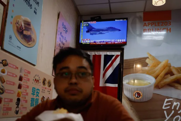 شخص يشاهد أخباراً عن إجراء الجيش الصيني تدريبات بالذخيرة الحية حول تايوان داخل متجر إفطار في تايبيه (إ.ب.أ)