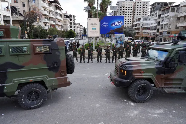 FILE PHOTO: Members of the Syrian Security forces stand guard near military vehicles on the day people protest in Latakia, Syria, December 28, 2025. REUTERS/Karam al-Masri/File Photo