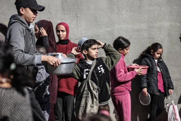 فلسطينيون في مخيم النصيرات وسط قطاع غزة ينتظرون تلقي وجبات الطعام يوم الثلاثاء (د.ب.أ)