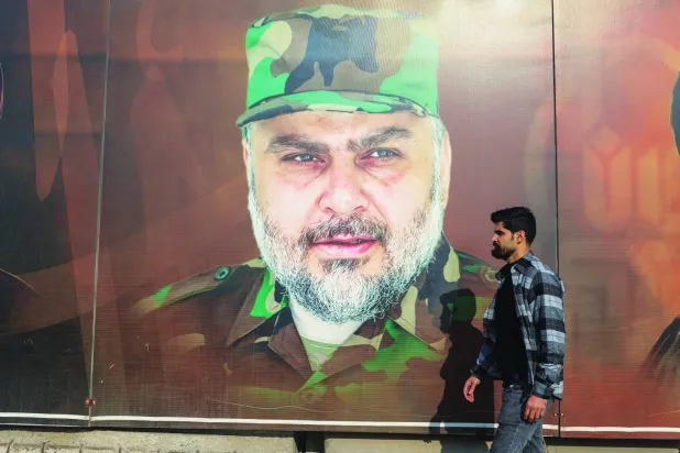عراقي بأحد شوارع بغداد يمر أمام صورة لمقتدى الصدر مرتدياً الزي العسكري الخاص بـ«سرايا السلام» (أ.ف.ب)