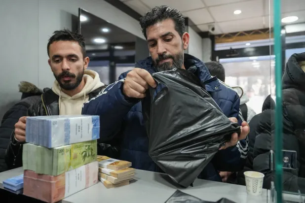 سوريون يستبدلون بالعملة القديمة العملة الجديدة في أحد مراكز الصرافة بدمشق (إ.ب.أ)