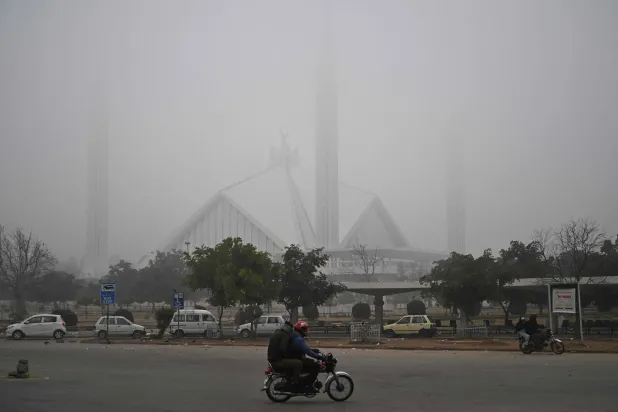  Commuters ride past the Faisal Mosque shrouded in fog on a cold winter morning in Islamabad on January 5, 2026. (AFP)