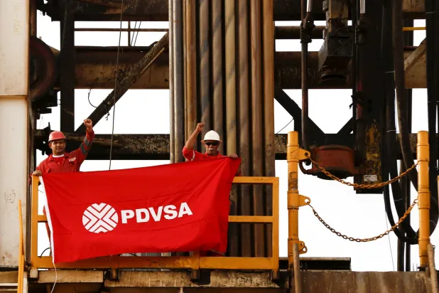 عاملان في حقل نفط يرفعان علماً يحمل شعار شركة النفط الحكومية الفنزويلية PDVSA (رويترز)