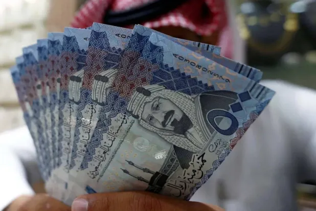 صراف سعودي يعرض أوراقاً نقدية بالريال السعودي في محل صرافة (رويترز)