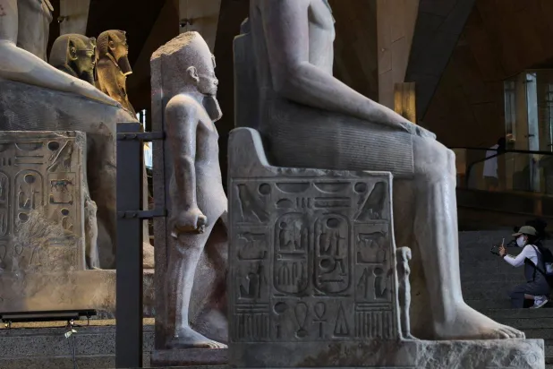 سائحة تلتقط صوراً لتماثيل معروضة داخل المتحف المصري الكبير والذي جذب العديد من السياح في 2025 (رويترز)