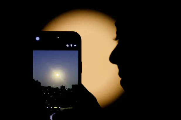امرأة تستخدم هاتفها الذكي لتصوير قمر الذئب أول قمر عملاق في عام 2026 وهو يضيء سماء القاهرة ليلاً (رويترز)