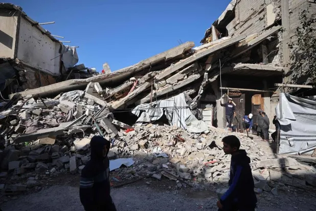 Palestinians walk past the debris of a collapsed house that was previously damaged by an Israeli strike, at the Maghazi refugee camp in the central of Gaza Strip on January 5, 2026. (AFP)