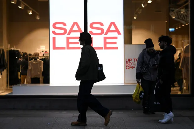 يمرّ أشخاص بجانب متجر يعرض لافتات تخفيضات في شارع أكسفورد بلندن (رويترز)