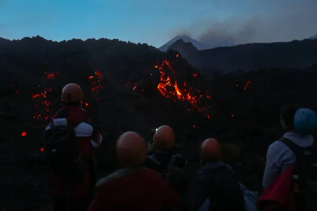 A group of people observes glowing lava emerging from a fissure during ongoing volcanic activity on Mount Etna in Catania, Sicily, Italy, January 3, 2026. REUTERS/Antonio Denti