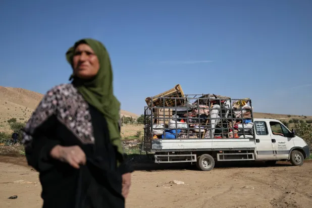 فلسطينية تقف قرب شاحنة تنقل متعلقات عائلاتها التي نزحت قسراً مع عائلات أخرى يوم الخميس من منطقة العوجا البدوية قرب أريحا بالضفة الغربية بعد تصاعد هجمات المستوطنين الإسرائيليين (رويترز)