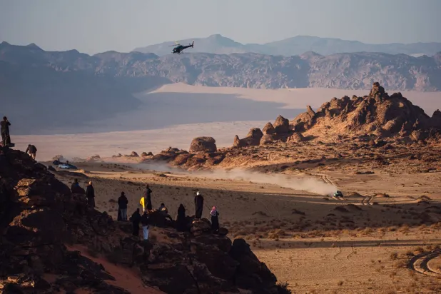 سيارة أحد المتسابقين تشق طريقها في حين يراقب عشاق الرالي المشهد من فوق إحدى الهضاب (الشرق الأوسط)