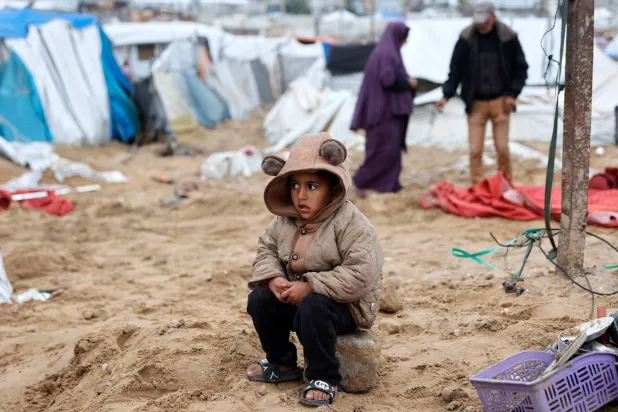 طفل فلسطيني يجلس على حجر فيما عائلته تعيد تنظيم الخيمة التي تؤويهم بعد قصف إسرائيلي استهدف مخيم الشاطئ للاجئين بمدينة غزة (أ.ف.ب)