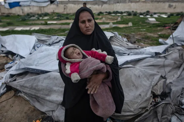 فلسطينية تحمل طفلها الرضيع بعد أن انهارت خيمتها في خان يونس جنوب قطاع غزة جراء الرياح القوية والأمطار (إ.ب.أ)