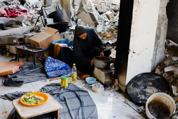 فلسطينية تطهو الطعام بين حطام منزلها في غزة (رويترز)