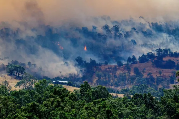 Smoke rises from a burning forest on a hillside behind a home near Longwood as bushfires continue to burn under severe fire weather conditions in Longwood, Victoria, Australia, January 9, 2026. AAP/Michael Currie via REUTERS 