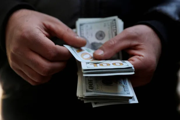 تاجر عملات يحمل أوراقاً نقدية من فئة المائة دولار مع انخفاض قيمة الريال الإيراني في طهران (رويترز)