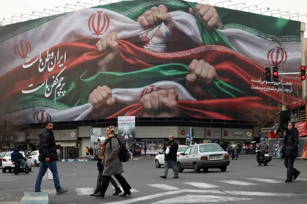 إيرانيون يسيرون بجوار لوحة إعلانية كُتب عليها «إيران وطننا» في «ساحة انقلاب» بطهران (إ.ب.أ)