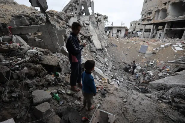 Filistinli çocuklar, Gazze Şeridi'nin merkezindeki Bureyc mülteci kampında bir çukurun yanında duruyor (AFP)